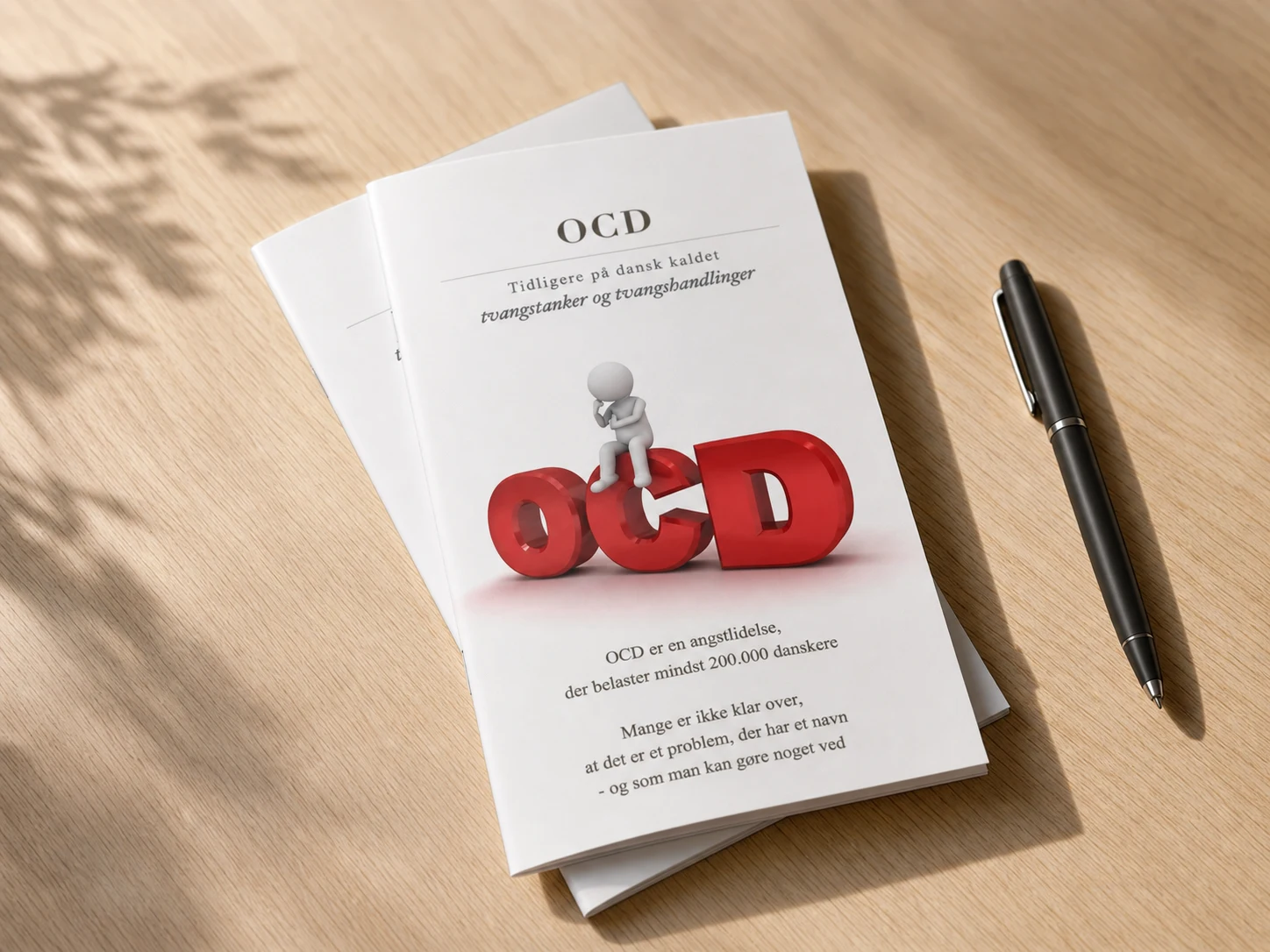 OCD-folderen ligger som trykt brochure på et lyst træbord ved siden af en pen